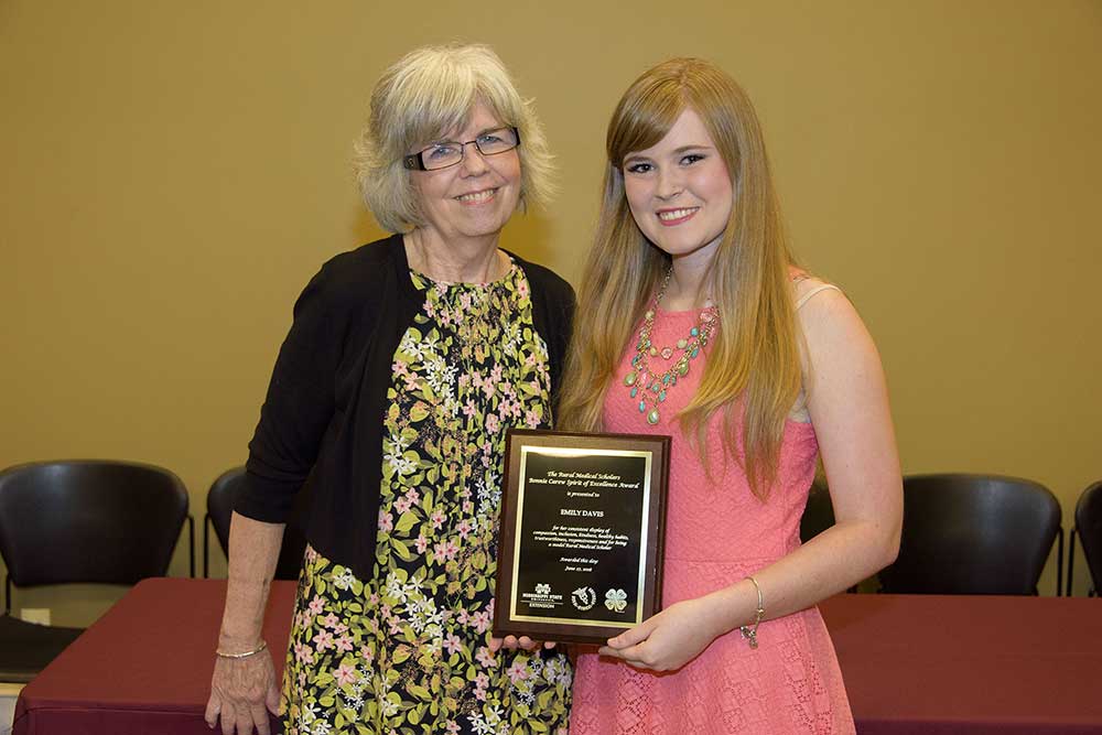 red-headed female holds award plaque standing next to another female.